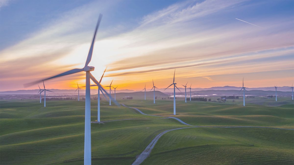 Parque eólico en un campo verde durante el atardecer, con un cielo despejado y colinas onduladas al fondo.