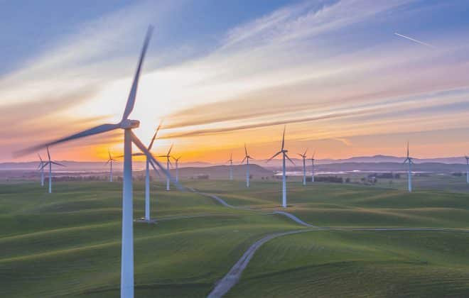 Parque eólico en un campo verde durante el atardecer, con un cielo despejado y colinas onduladas al fondo.