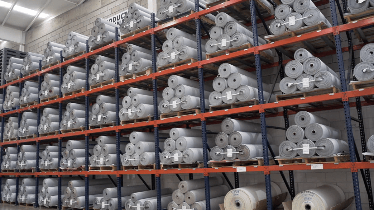 Estanterías de almacenamiento en un almacén, llenas de rollos de material de vinilo gris.