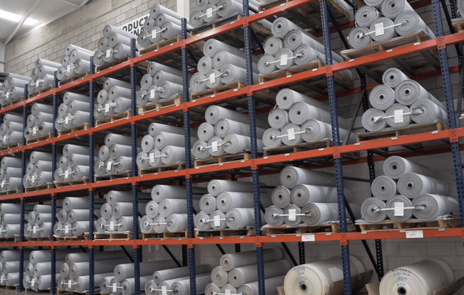 Estanterías de almacenamiento en un almacén, llenas de rollos de material de vinilo gris.